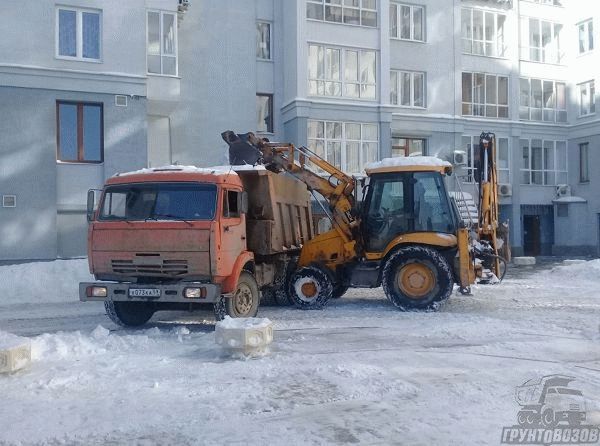 Фронтальный погрузчик загружает снег на грузовик Камаз на ровном дворе